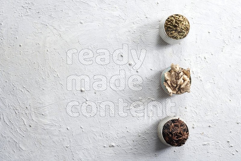 Cardamom, ginger and star anise in 3 bowls on a textured white background