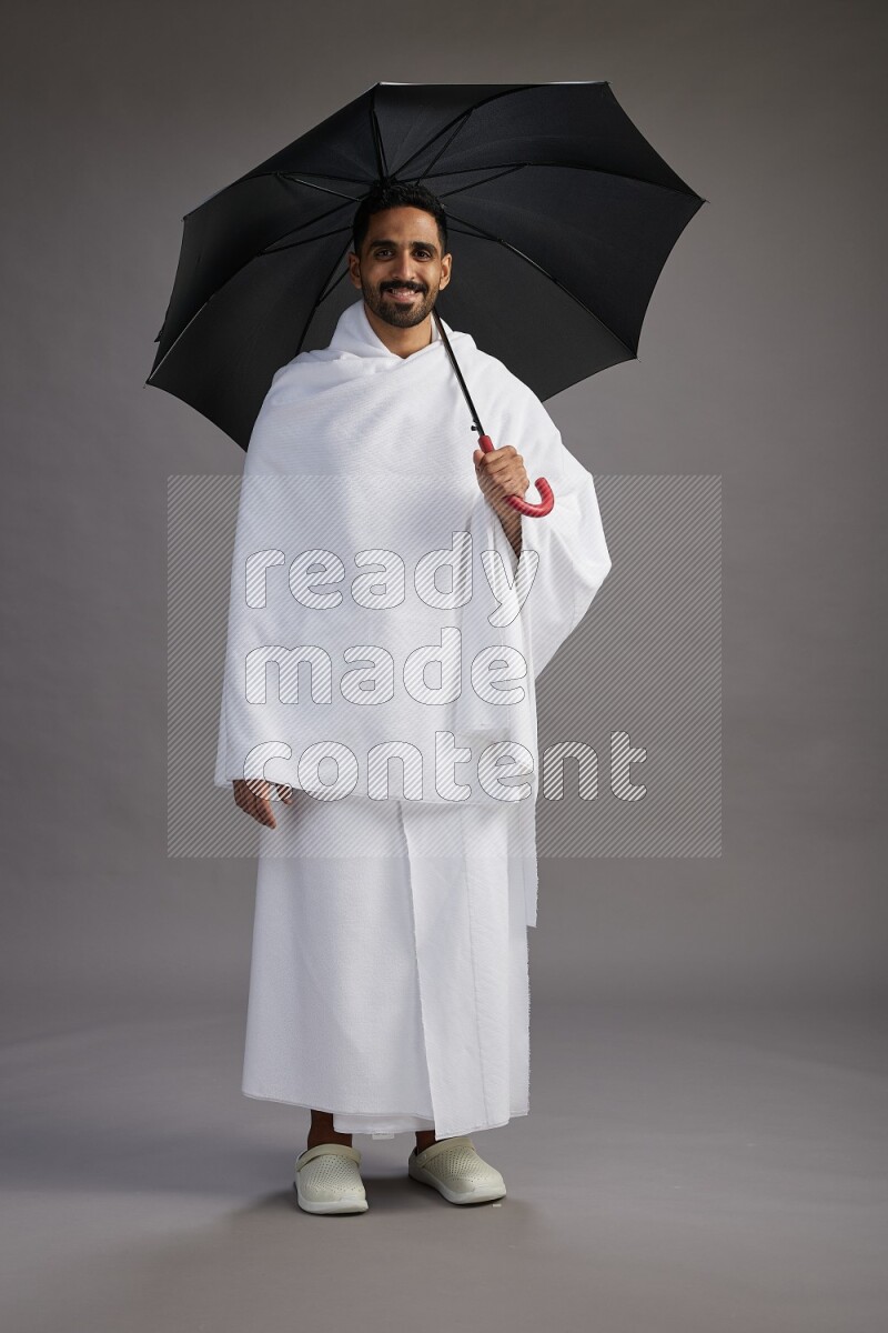 A man wearing Ehram Standing holding umbrella on gray background