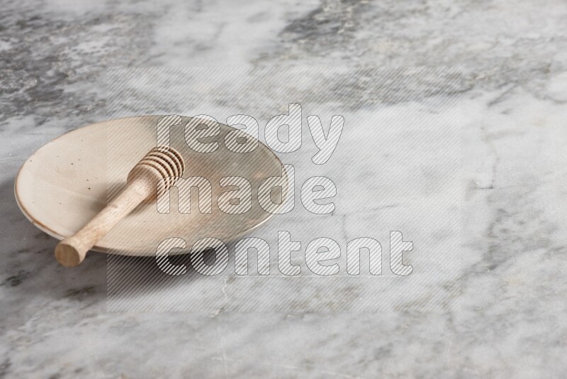 Multicolored pottery plate with wooden honey dipper in it on grey marble background