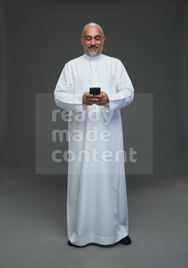 Saudi man without shomag Standing texting on phone on gray background