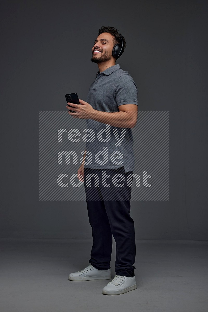 A man wearing casual and using his phone and headphone eye level on a gray background