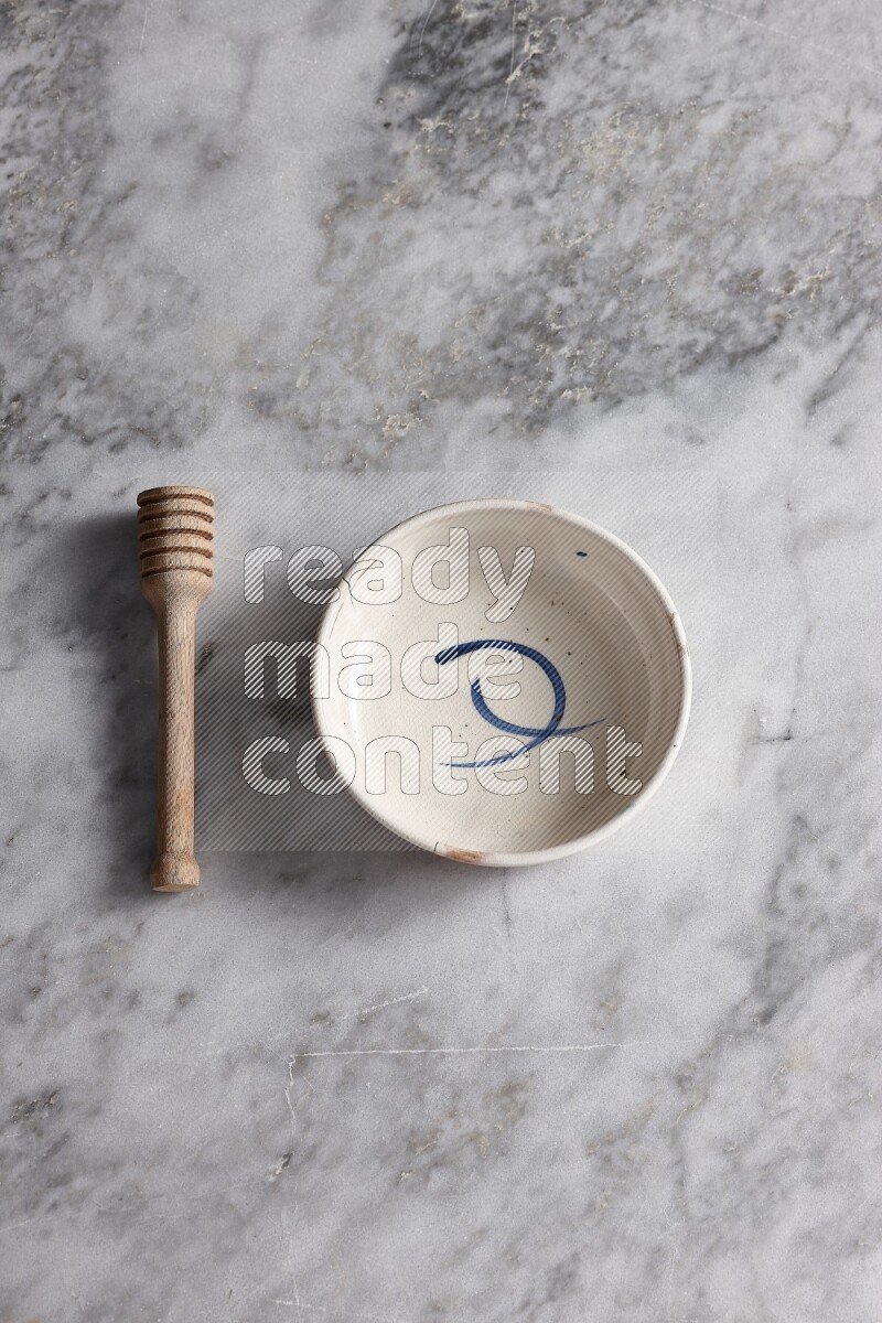 Multicolored pottery bowl with wooden honey dipper on the side on grey marble background
