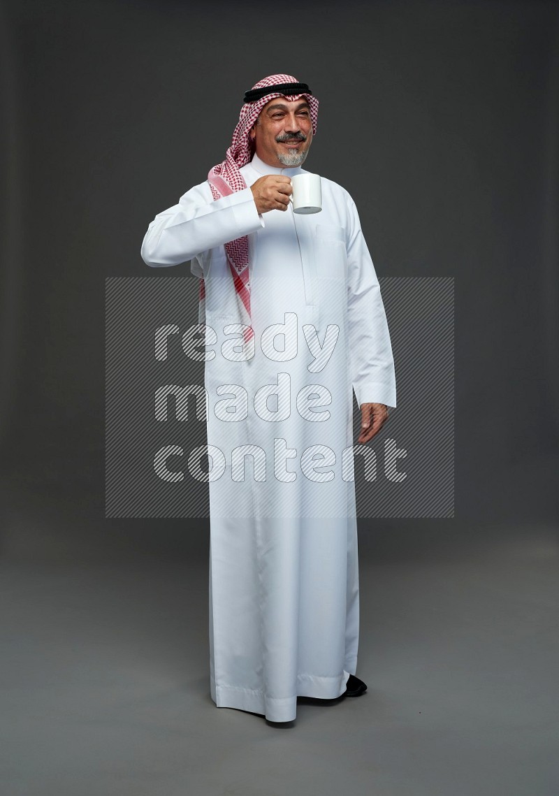 Saudi man with shomag Standing holding mug on gray background