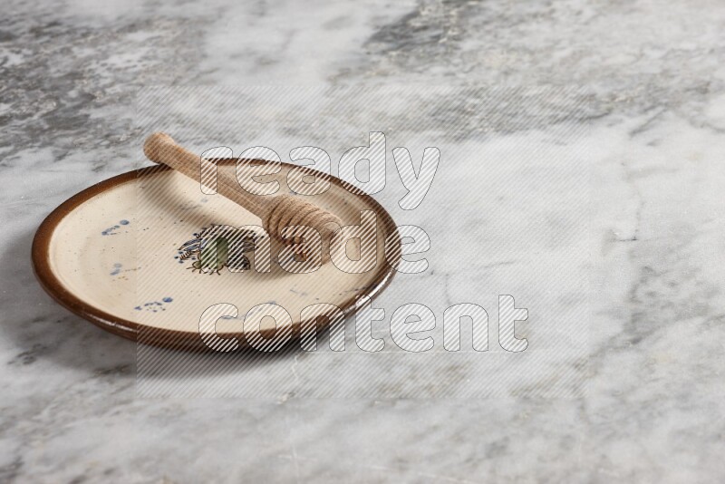 Decorative pottery plate with wooden honey dipper in it on grey marble background