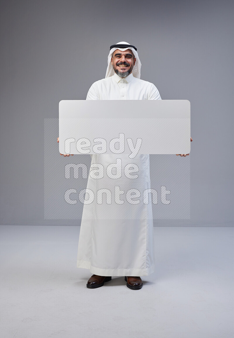 Saudi man Wearing Thob and white Shomag standing holding board on Gray background