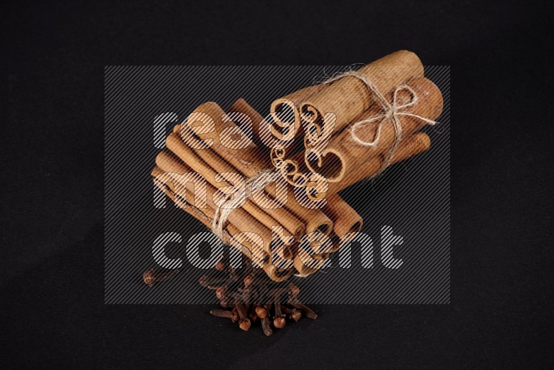 Two bounded stacks of cinnamon sticks with cloves on black background