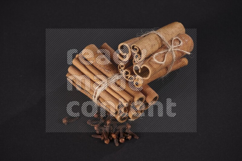Two bounded stacks of cinnamon sticks with cloves on black background
