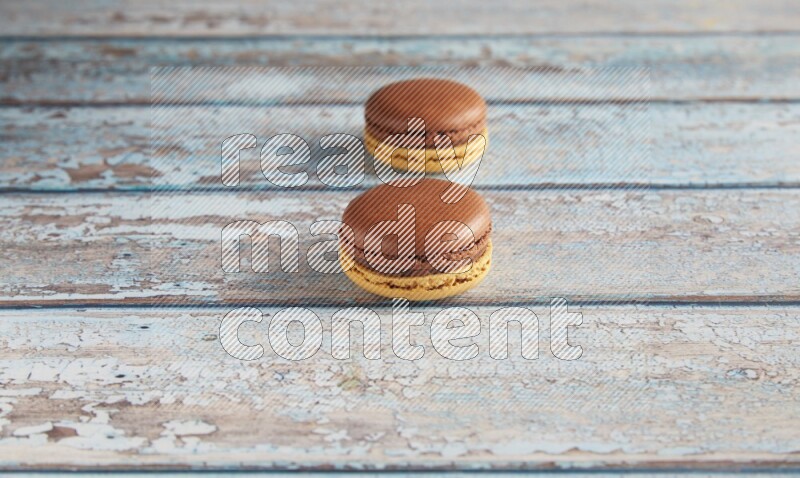 45º Shot of two Yellow and Brown Chai Latte macarons on light blue wooden background