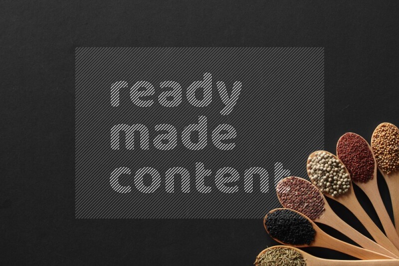 wooden spoons filled with white peppers, mustard seeds, black seeds, garden cress, cumin and flax on black flooring