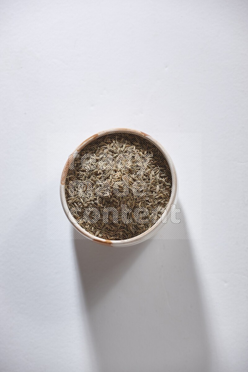 A beige bowl full of cumin seeds on a white flooring
