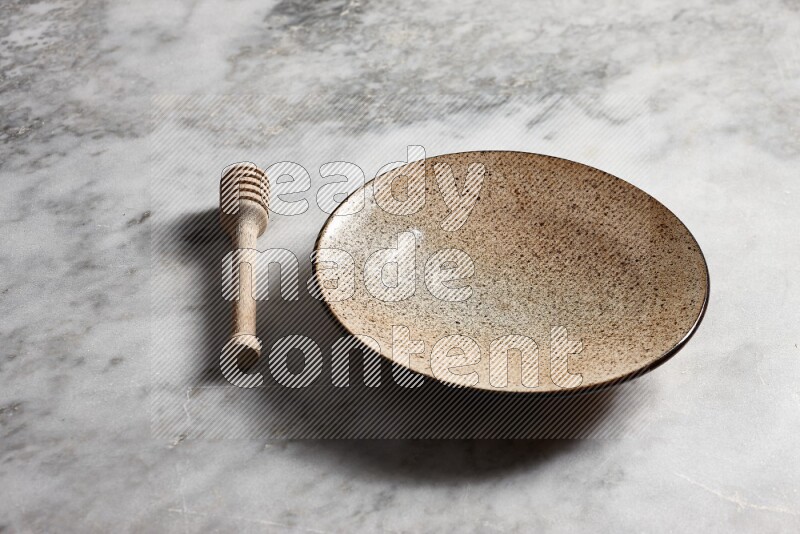 Multicolored pottery plate with wooden honey dipper on the side on grey marble background