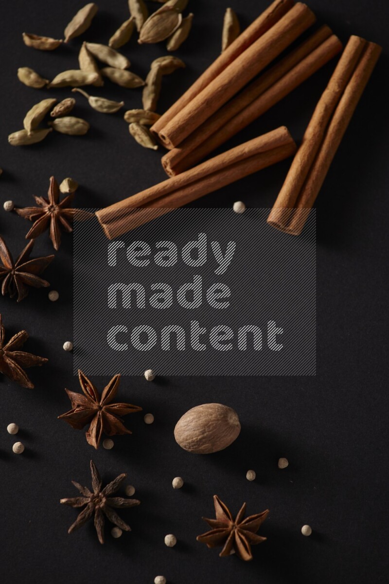 أعواد من القرفة وحبوب الهيل واليانسون النجمي وجوزة الطيب وحبوب الفلفل الأبيض علي خلفية سوداء