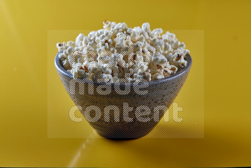 A multicolored pottery bowl full of popcorn on a yellow background in different angles