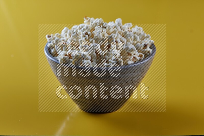 A multicolored pottery bowl full of popcorn on a yellow background in different angles