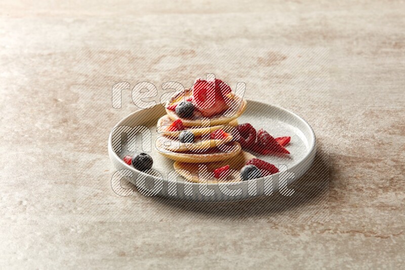 Five stacked mixed berries mini pancakes in a blue plate on beige background