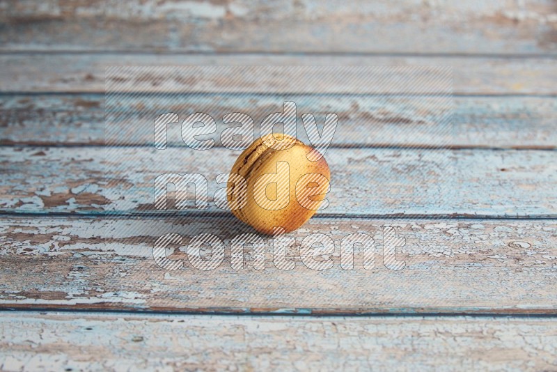 45º Shot of Yellow Crème Brulée macaron on light blue wooden background