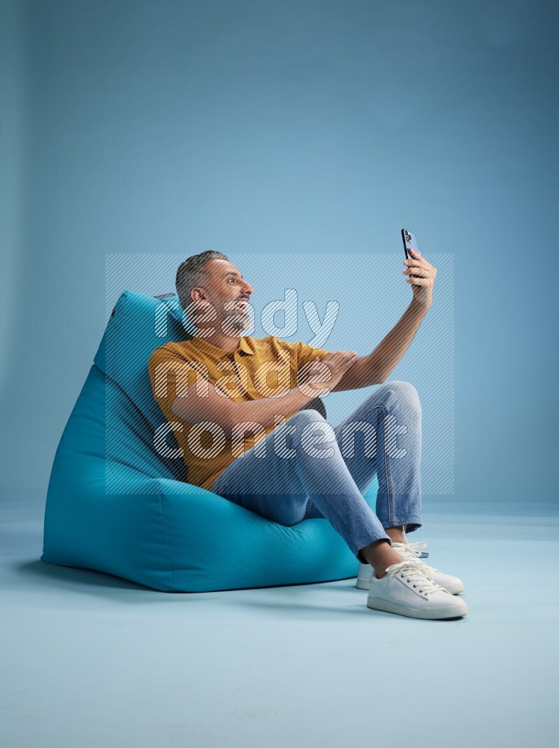 A man sitting on a blue beanbag and taking selfie