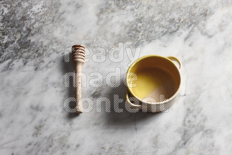 Multicolored Pottery bowl with wooden honey handle on the side with grey marble flooring, 65 degree angle