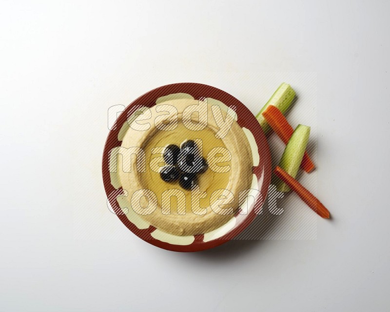 Hummus in a traditional plate garnished with black olives on a white background