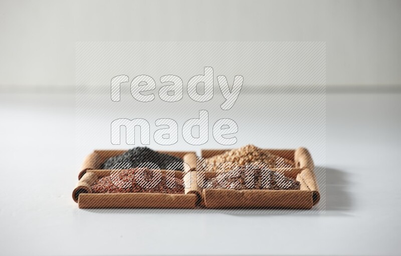 4 مربعات من أعواد القرفة ممتلئة بحبة البركة وبذور الخردل وبذور الكتان وحب الرشاد على أرضية بيضاء