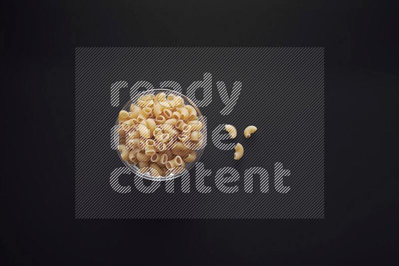 Elbow pasta in a glass bowl on black background