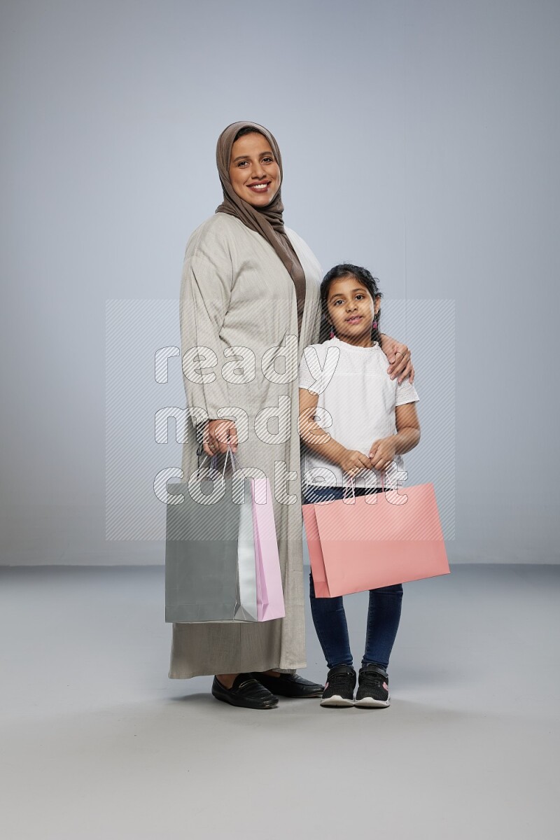 Mom and daughter holding shopping bags on gray background