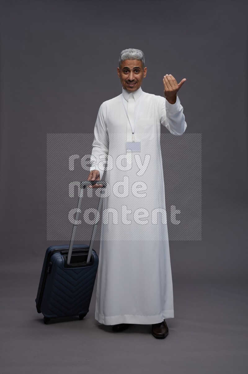 Saudi man wearing thob with neck strap employee badge standing holding bag on gray background