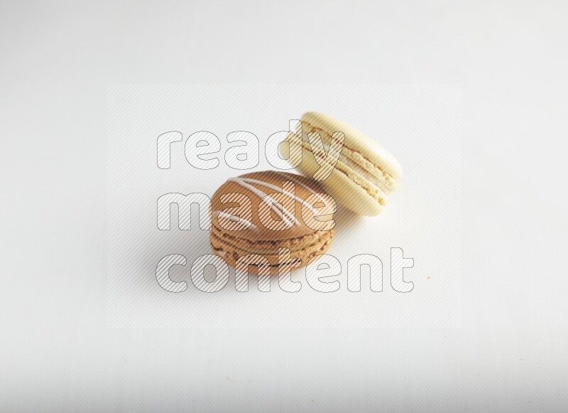 45º Shot of of two assorted Brown Irish Cream, and Yellow Vanilla macarons on white background