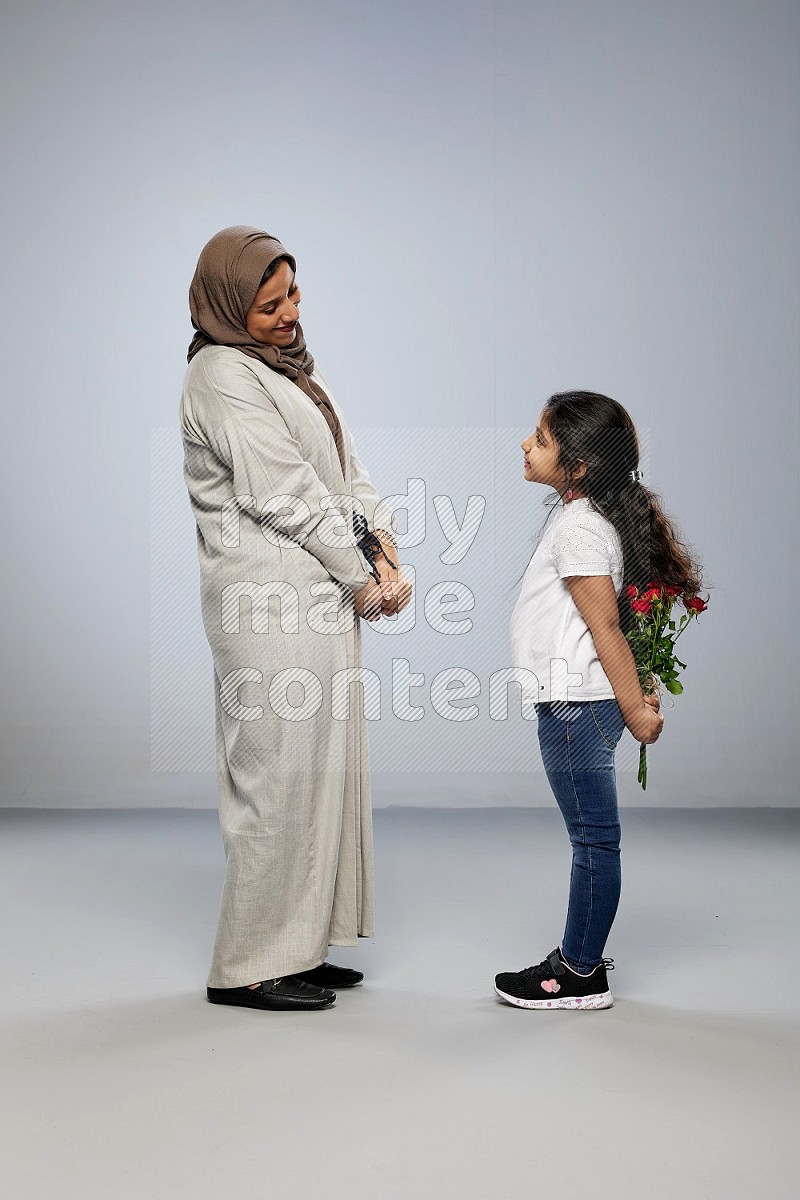 A girl standing giving flowers to her mother on gray background