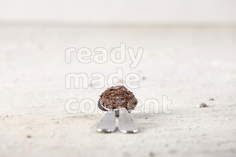 2 metal spoons full of flax seeds on a textured white flooring