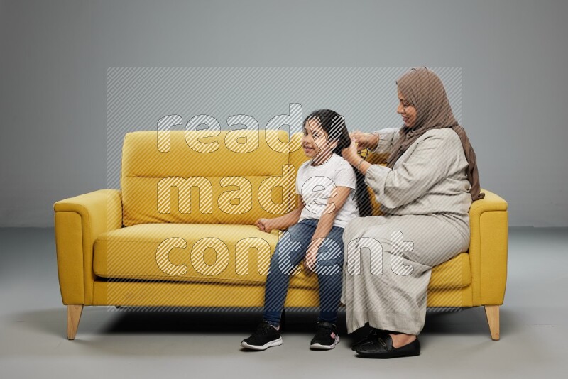 A mother sitting styling hair for her daughter on gray background