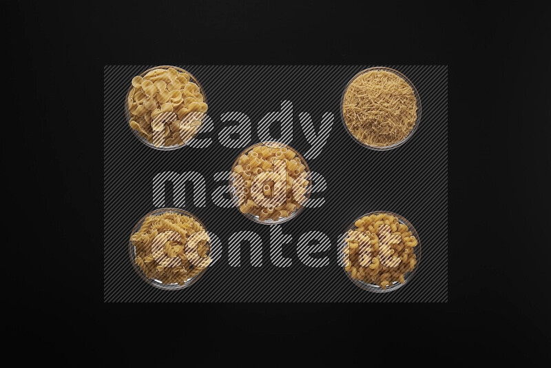 Different pasta types in 5 glass bowls on black background