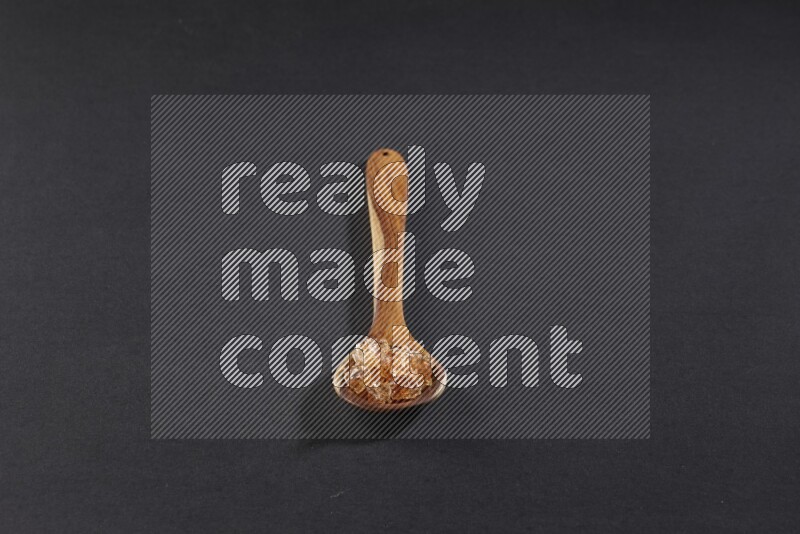 A wooden ladle filled with gum arabic on black flooring