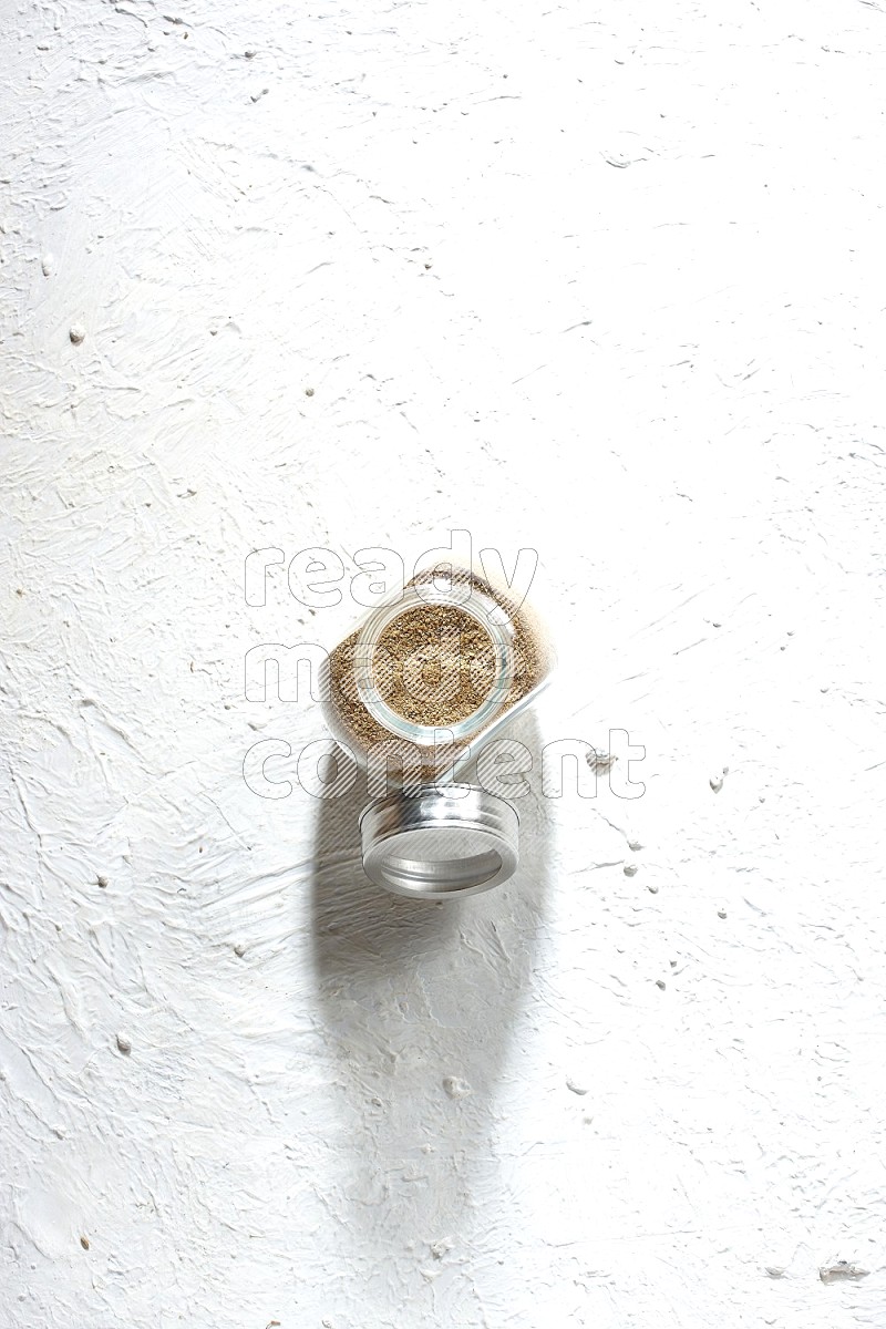 وعاء زجاجي ممتلئ ببودرة الكمون على خلفية بيضاء