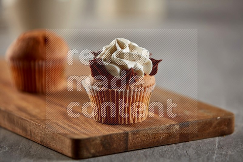 Vanilla cupcake topped with cream on a wooden board