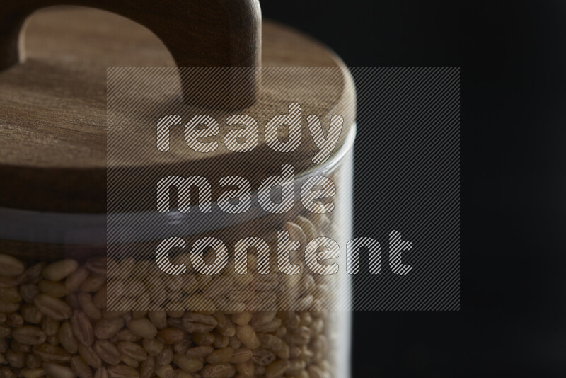 Hulled wheat in a glass jar on black background
