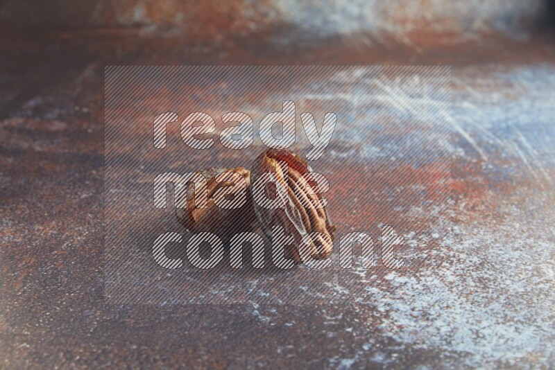 two pecan stuffed madjoul dates on a rustic reddish background