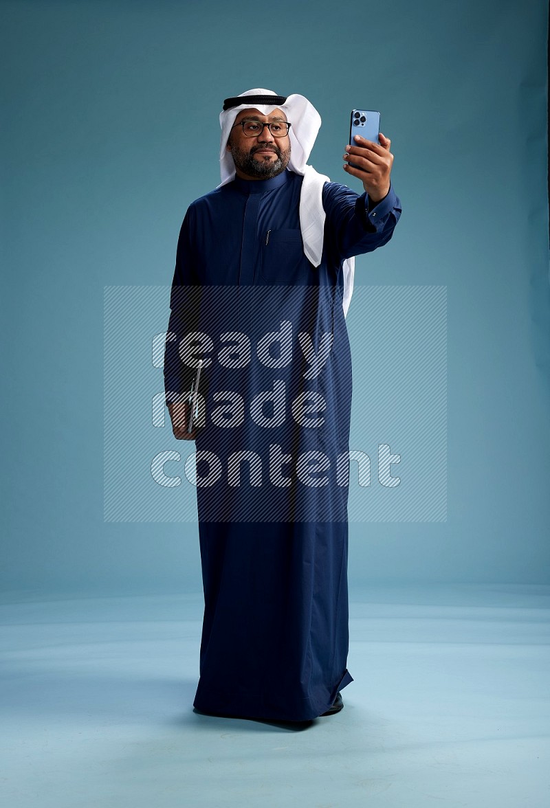 Saudi Man with shimag Standing taking selfie on blue background