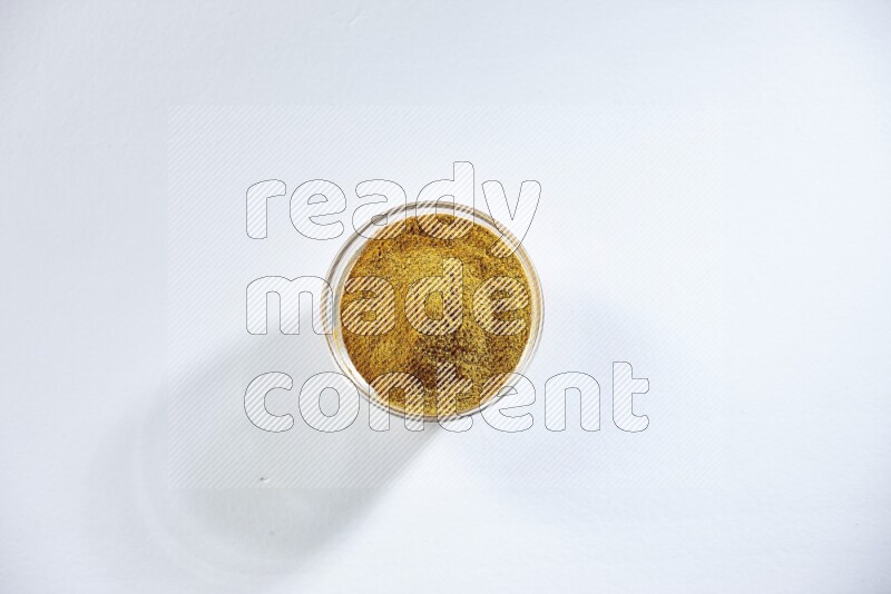 A glass bowl full of turmeric powder on white flooring