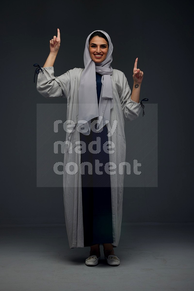 A Saudi woman wearing a light gray Abaya and head scarf standing and making multi poses eye level on a grey background