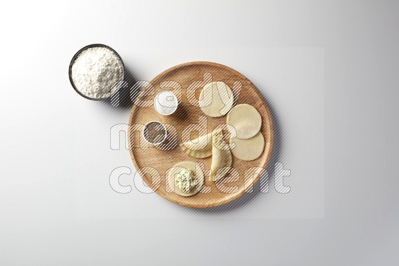 two closed sambosas and one open sambosa filled with cheese while flour, salt, and black pepper aside in a wooden dish on a white background