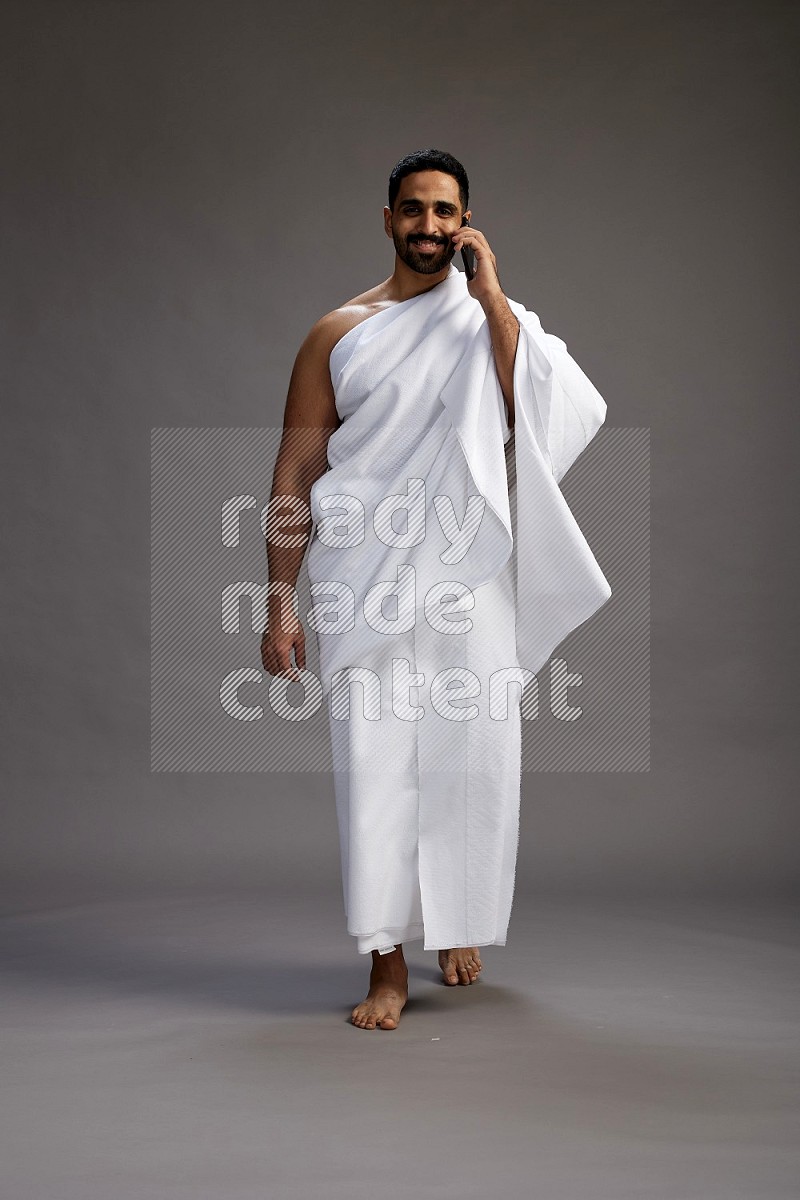 A man wearing Ehram Standing talking on phone on gray background