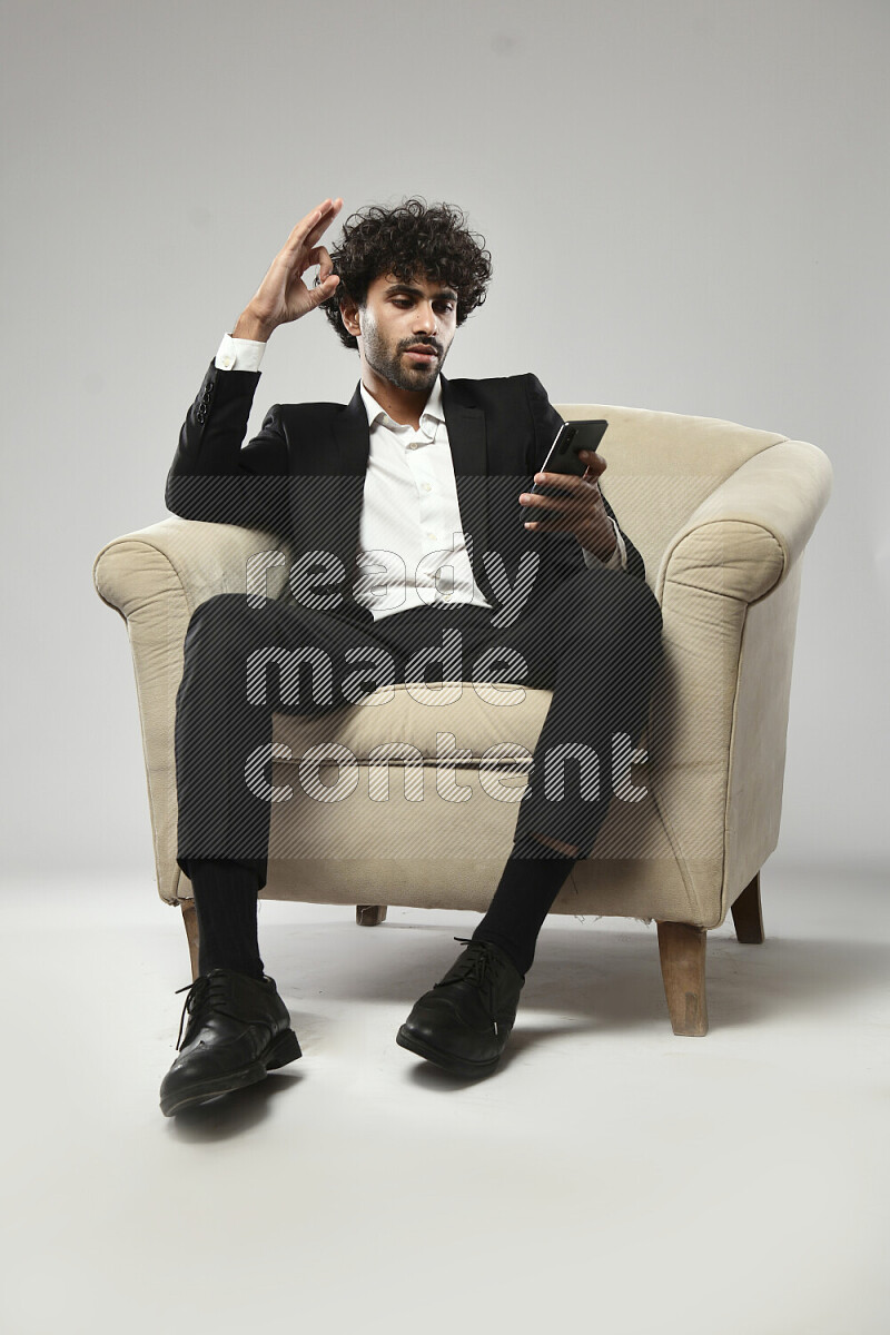 رجل يرتدي ملابس رسمية يجلس علي كرسي و يتصفح الهاتف علي خلفية بيضاء