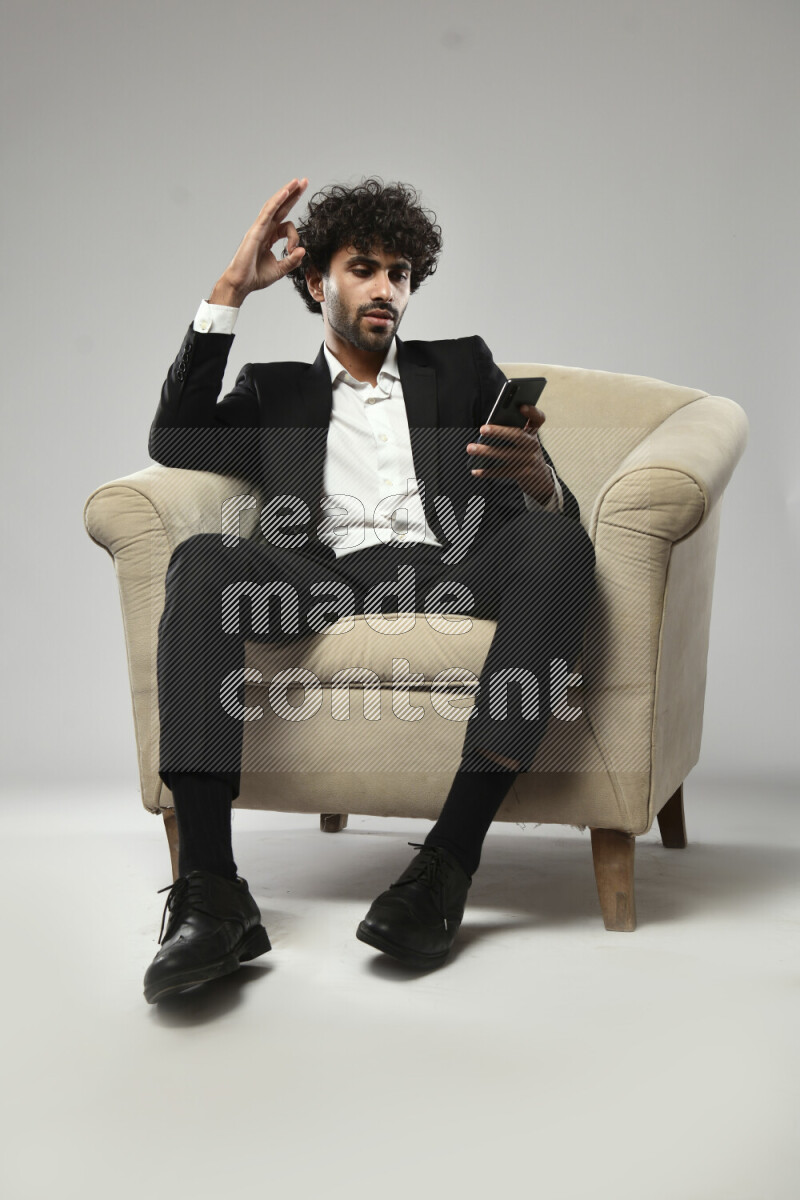 A man wearing formal sitting on a chair browsing on the phone on white background