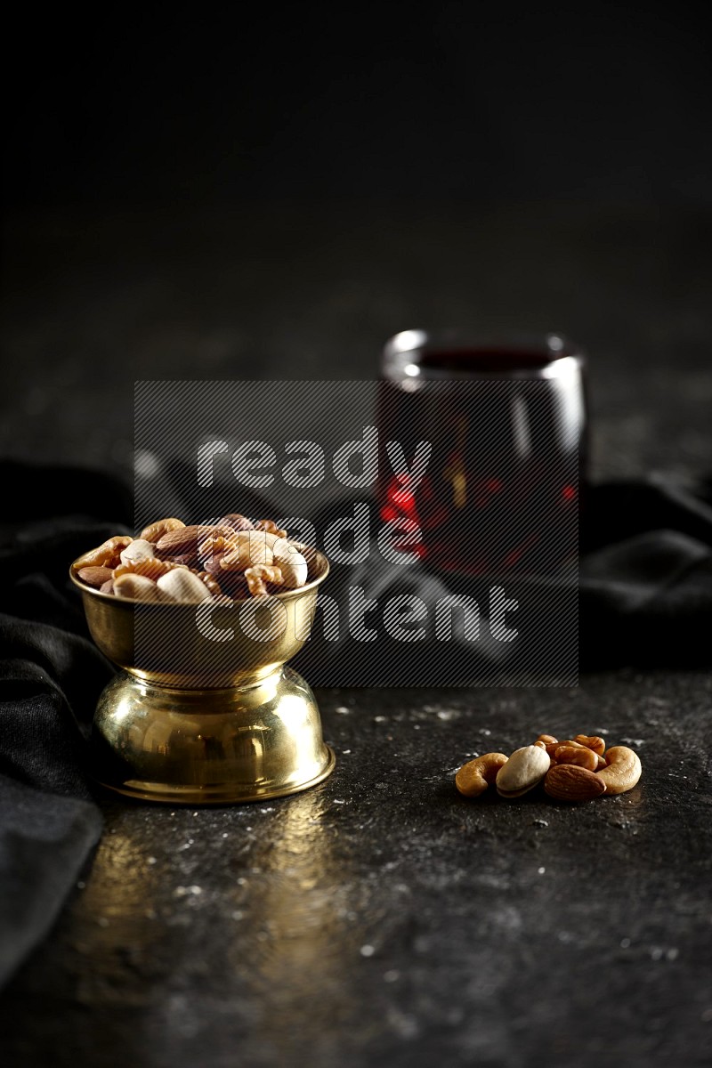 Nuts in a metal bowl with hibiscus and a napkin in a dark setup