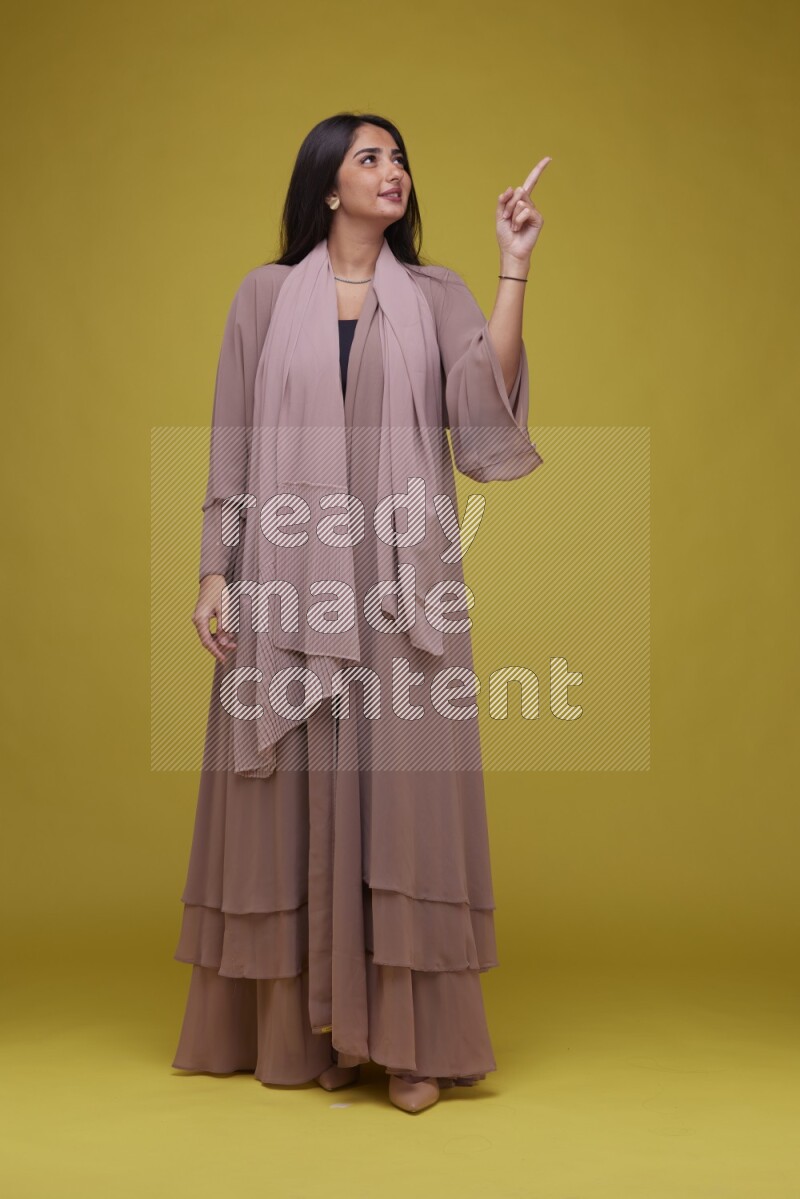A woman Pointing on a Yellow Background wearing Brown Abaya