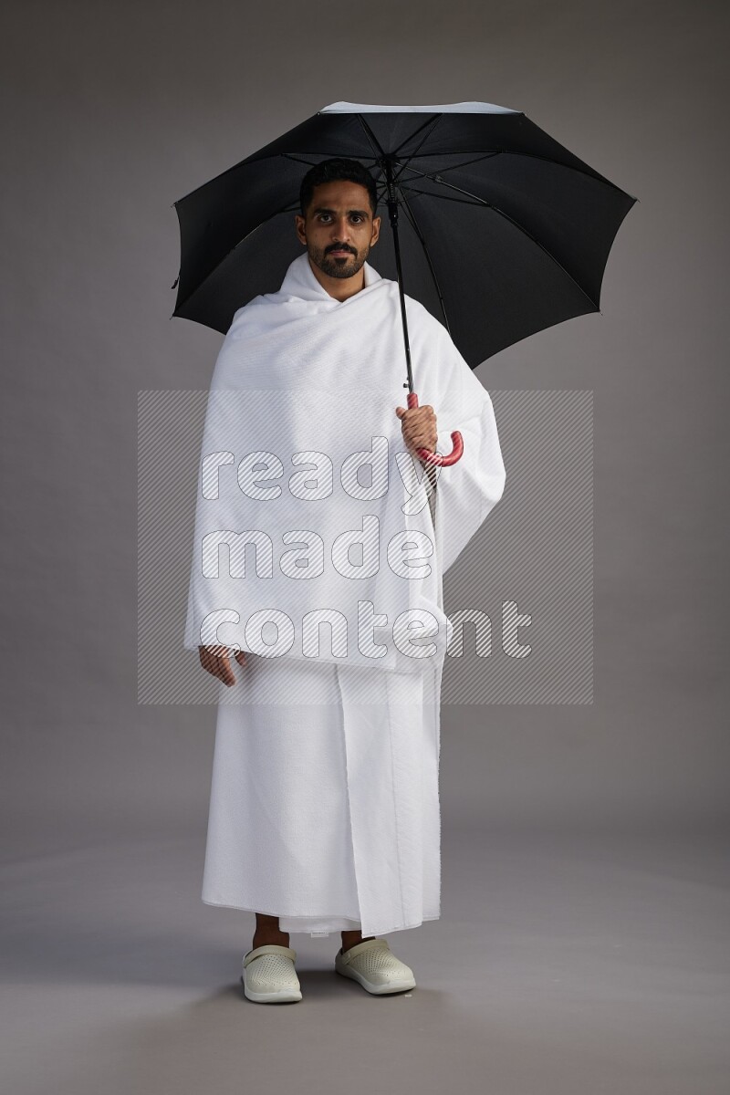 A man wearing Ehram Standing holding umbrella on gray background
