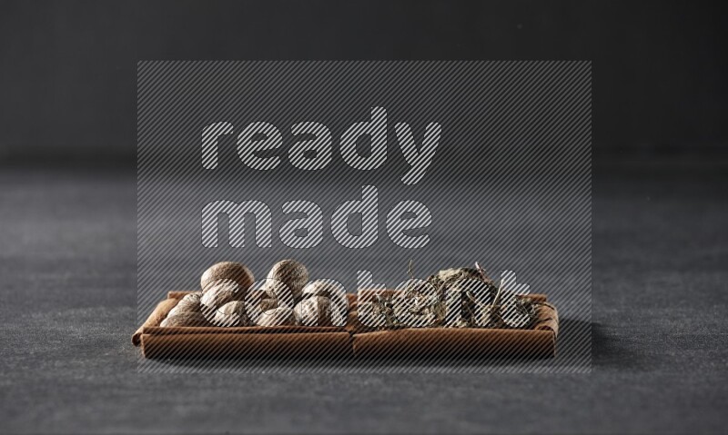 مربعان من أعواد القرفة ممتلئان بجوزة الطيب والريحان المجفف علي خلفية سوداء