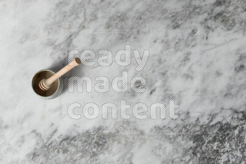 Multicolored pottery bowl with wooden honey dipper in it on grey marble background