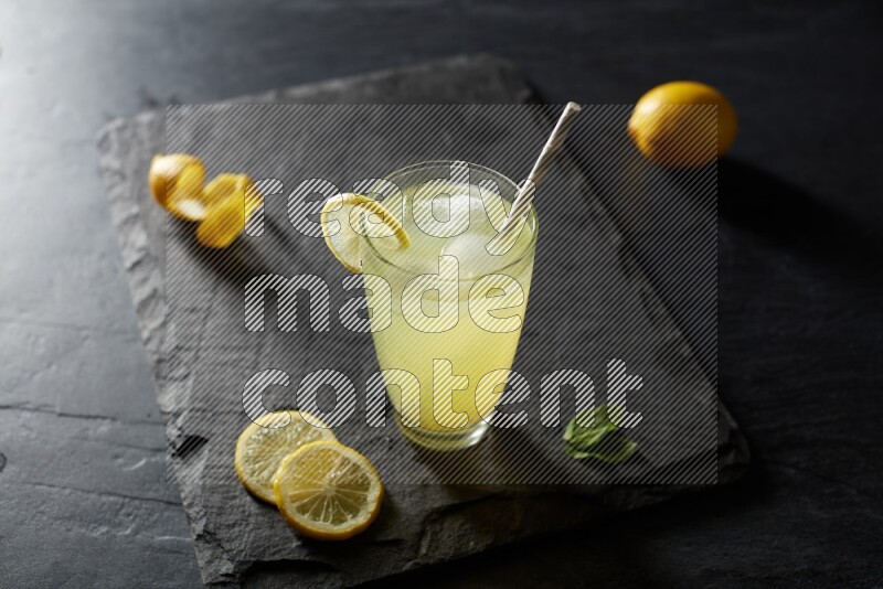 A glass of lemon juice with a straw on black background